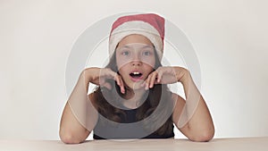 Beautiful happy girl teenager in a Santa Claus hat look and emotionally expresses a surprise on white background
