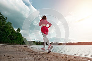 A beautiful, happy girl in a tracksuit runs along the path of a lake or sea. The concept of a healthy lifestyle, cardio workout.
