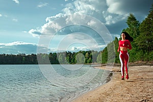 A beautiful, happy girl in a tracksuit runs along the path of a lake or sea. The concept of a healthy lifestyle, cardio workout.