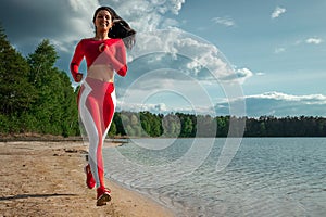 A beautiful, happy girl in a tracksuit runs along the path of a lake or sea. The concept of a healthy lifestyle, cardio workout.