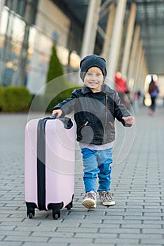 Beautiful happy girl travels with stylish suitcase. Little child traveler goes to the trip from airport.