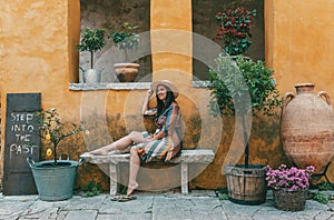 Portrait of woman wearing hat and dress, sitting in front of old orange building