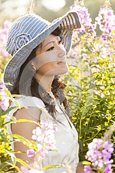 Beautiful, happy, healthy, sensual, sexy, young Asian woman enjoying summer sunlight in a flower garden. She is wearing a sun hat