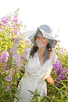 Beautiful, happy, healthy, smiling, young Asian woman picking flowers outdoors in summer. She is wearing a feminine dress and sun