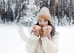 A beautiful happy laughing young girl in gloves and a winter hat-scarf, covered with snow flakes. Winter forest