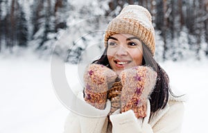 A beautiful happy laughing young girl in gloves and a winter hat-scarf, covered with snow flakes. Winter forest