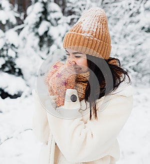 A beautiful happy laughing young girl in gloves and a winter hat-scarf, covered with snow flakes. Winter forest