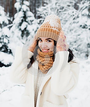 A beautiful happy laughing young girl in gloves and a winter hat-scarf, covered with snow flakes. Winter forest