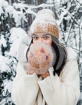 A beautiful happy laughing young girl in gloves and a winter hat-scarf, covered with snow flakes. Winter forest