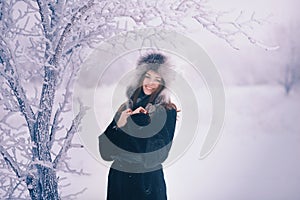 Beautiful happy laughing young woman wearing winter hat gloves covered with snow flakes.