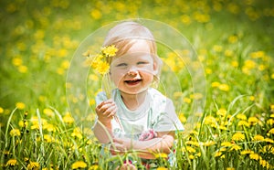 Beautiful happy little baby girl sitting on a green meadow with yellow flowers dandelions