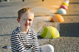 Beautiful happy little boy sitting on colored stones, looking at camera