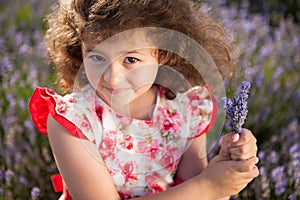 Beautiful happy little girl with bouquet of summer flowers in lavender field