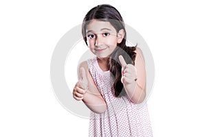 Beautiful happy little girl with long dark hair and dress looking at camera with thumbs up.