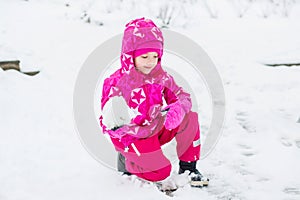 Beautiful happy little girl in pink winter clothes playing
