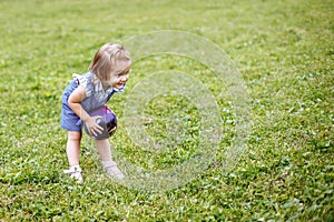 Beautiful happy little girl playing with a ball on a green meadow in the nature in the Park