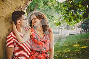 Beautiful happy loving couple in red clothes on nature under a big tree embracing and looking at each other