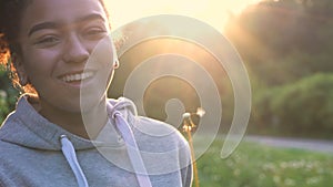 Beautiful happy mixed race African American girl teenager or young woman blowing a dandelion at sunset or su