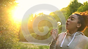 Beautiful happy mixed race African American girl teenager or young woman laughing, smiling and blowing a dandelion