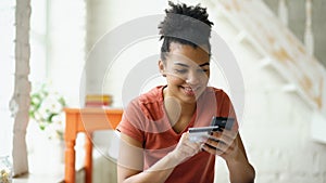 Beautiful happy mixed race woman online banking using smartphone shopping online with credit card at home lifestyle