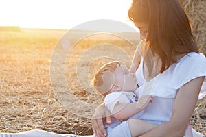 Beautiful happy mother breastfeeding her baby boy outdoor.