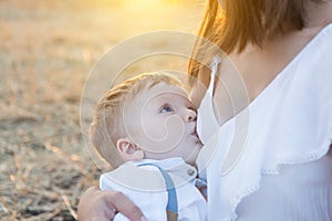 Beautiful happy mother breastfeeding her baby boy outdoor.