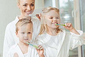 beautiful happy mother and children in bathrobes brushing photo