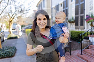 Beautiful happy mother holding her cute baby in peaceful neighborhood