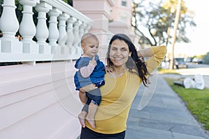 Beautiful happy mother holding her cute baby in peaceful neighborhood