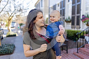 Beautiful happy mother holding her cute baby in peaceful neighborhood