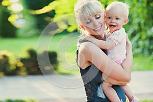 Beautiful happy mother hugging baby girl with love outdoors summer background