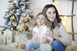 Beautiful happy mother with lher ittle daughter in knit sweater sitting on the background of Christmas interior