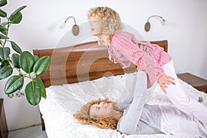 Beautiful happy mother is lying on the bed and raising her daughter