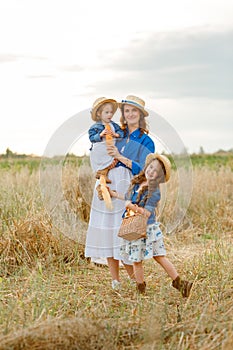 Beautiful happy mother in a straw hat with two little cute daughters standing in the middle of a bread field on a sunny summer day