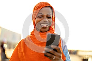 Beautiful, happy Muslim woman using smartphone outdoors