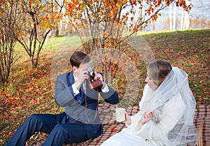 Beautiful happy newly married couple sitting on plaid in park, g