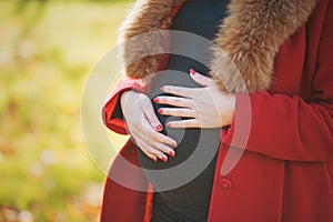 Beautiful happy pregnant woman staying in autumn park touching her belly and enjoying expecting of baby.