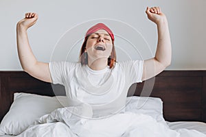 Beautiful happy redhead woman waking up in her bed, smiling and stretching, copy space. Millennial Caucasian girl