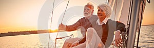 Beautiful and happy senior couple in love sitting on the side of sailboat or yacht deck floating in sea at sunset and