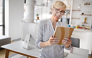 Beautiful happy senior woman using tablet computer at home