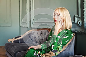 Beautiful happy smiling blonde woman in green dress sitting on velvet sofa