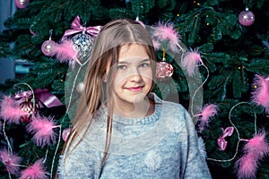 Beautiful happy smiling girl with long hair, wearing gray jumper, posing near Christmas tree