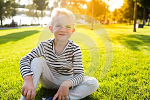 Beautiful happy smiling little boy sit on grass looking at camera