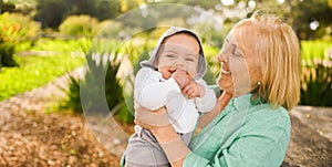 Beautiful happy smiling senior elderly woman holding on hands cute little baby boy. Grandmother and grandson having fun