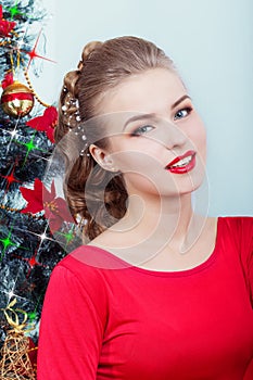 Beautiful happy smiling young woman in evening dress with bright makeup with red lipstick sitting near the Christmas tree