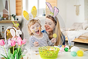 Beautiful happy son and mother in headbands with bunny ears decorate eggs with a brush and bright paints, prepare to