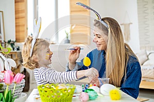 Beautiful happy son and mother in headbands with bunny ears decorate eggs with a brush and bright paints, prepare to