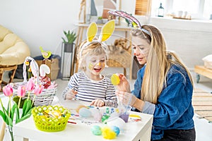 Beautiful happy son and mother in headbands with bunny ears decorate eggs with a brush and bright paints, prepare to