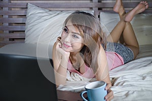 Beautiful and happy student woman enjoying on bed with laptop computer watching internet movie or having video chat call with frie