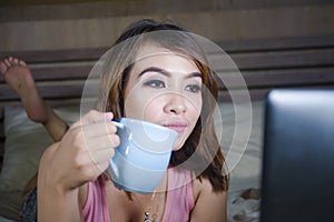 Beautiful and happy student woman enjoying on bed with laptop computer watching internet movie or having video chat call with frie